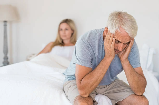 Tired middle-aged man sitting on the edge of the bed, showing signs of low energy