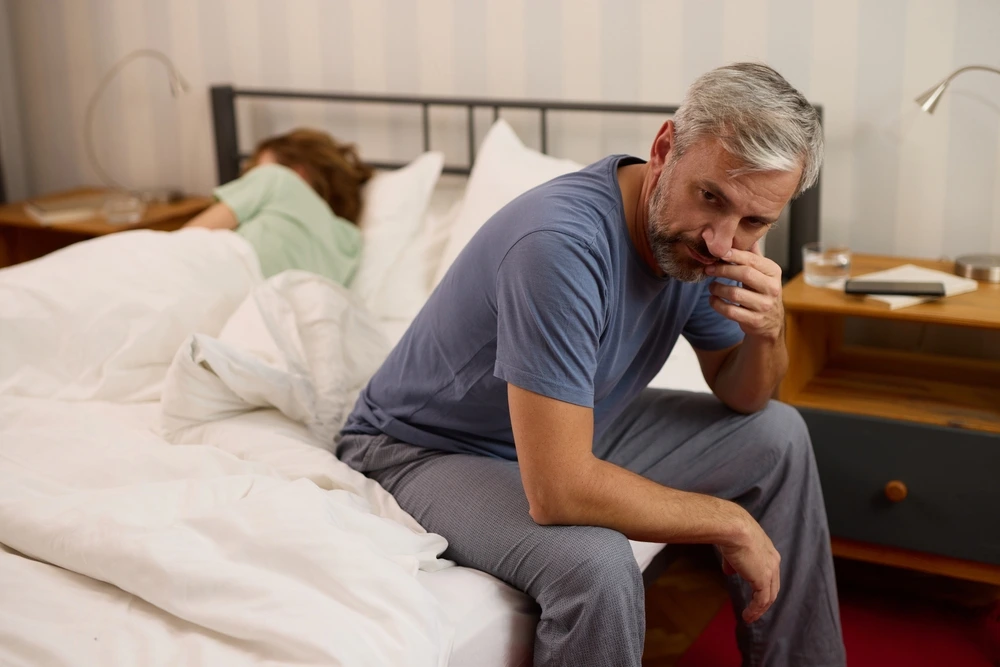 Man sitting awake on the edge of the bed at night, unable to sleep